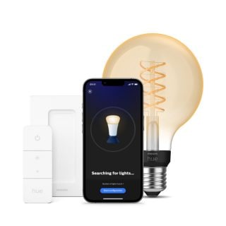 A collection of smart lighting products including a white wall switch, a smartphone with setup screen, and a large bulb with visible filament.