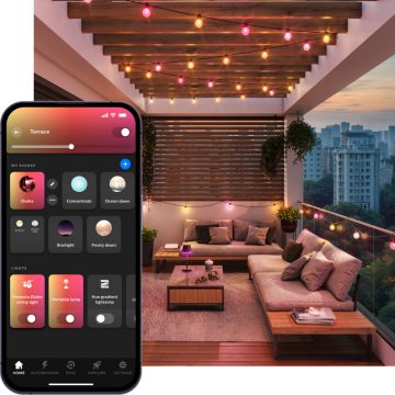 Una zona para sentarse en el balcón por la noche iluminada con guirnaldas de bombillas de fiesta globo para exterior: luz inteligente en tonos rosas y amarillos. 