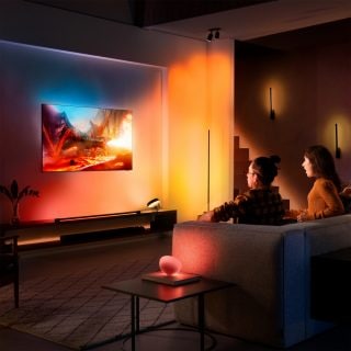 Pareja sentada en el sofá viendo la televisión con luces rojas, naranjas y amarillas