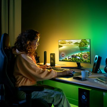 Nainen istuu vihreällä ja keltaisella Philips Hue ‑älyvaloilla valaistun pelipöydän ääressä