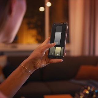 Une personne contrôle l'éclairage connecté Philips Hue à l'aide de l'application Hue sur un smartphone.