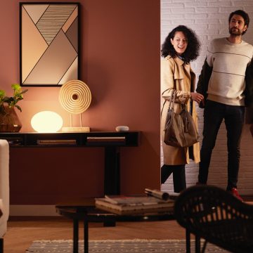 Un couple entre dans un salon éclairé par une lampe intelligente Philips Hue qui émet une lumière intelligente blanc chaud.