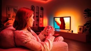 Une femme jouant sur son téléviseur avec un système d’éclairage de spectacle immersif, diffusant des lumières connectées rouges, orange et blanches.