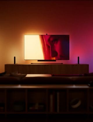 Une configuration d’éclairage de divertissement pour salon et téléviseur éclairée par des bandes lumineuses à dégradé qui brillent dans des tons jaune, orange et violet. 