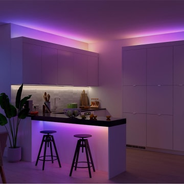 Des bandes lumineuses Essentiel Hue dissimulées derrière des éléments de cuisine et un comptoir produisant un effet d’éclairage mural dans une lumière diffuse blanche, jaune, rose et violette. 