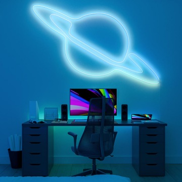 Une bande lumineuse flexible Essentiel Hue pliée en forme de planète installée au-dessus d’un bureau avec un ordinateur et projetant un éclairage blanc et bleu pâle. 