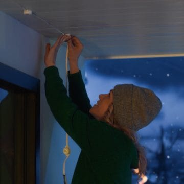 Une femme installe une guirlande blanche de lumières d’extérieur permanentes Festavia.