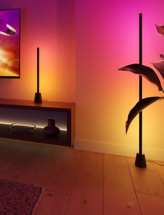 Une lampe de table et un lampadaire Philips Hue Play, placés à côté d’une TV, créent des effets d'éclairage immersifs dans des dégradés de lumière violets, roses, jaunes et bleus. 