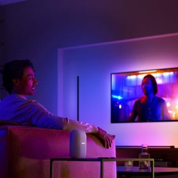 Homme sur un canapé regardant la télévision avec un éclairage et un haut-parleur intelligent surround sur la table d'appoint à côté de lui