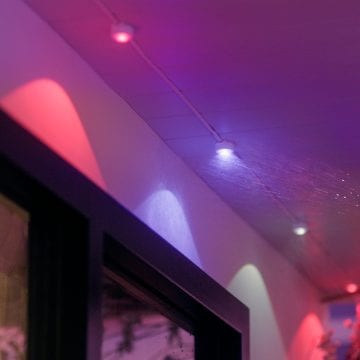 Une guirlande de lampes permanentes Festavia fixée au plafond d'un balcon, avec des modules d'éclairage diffusant une lumière rose et violette
