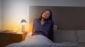 Femme se réveillant dans une chambre avec un réveil lumière connecté simulant le lever de soleil pour un démarrage en douceur de la journée 