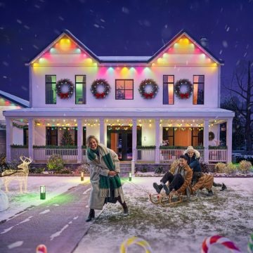 Une famille passe un moment agréable devant la maison dont la façade est illuminée par des lampes d'extérieur permanentes Festavia qui brillent de plusieurs couleurs sur le thème de Noël. 