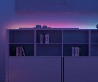 Un salotto e un allestimento di illuminazione per l'intrattenimento televisivo illuminati da strisce LED intelligenti che brillano con sfumature nei toni del viola e del blu. 