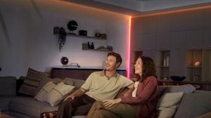 Una coppia seduta su un divano in un soggiorno con angoli e linee del soffitto illuminati dalla luce diretta di una striscia LED OmniGlow. 