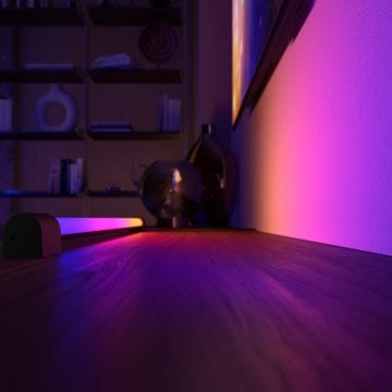 Hue gradient light tube가 파란색 톤, 핑크색 톤, 보라색 톤 및 노란색 톤이 혼합된 스마트 조명으로 벽 전체를 비추고 있는 모습.