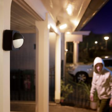 옥외 동작 센서에 연결된 두 벽등이 켜 있는 정문으로 다가가는 한 남성.