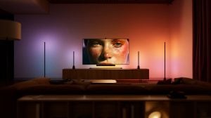 Een entertainmentopstelling in de woonkamer met Philips Hue Play vloer- en tafellampen aan weerszijden van een tv, gesynchroniseerd met het scherm om paarse, oranje en roze lichteffecten op de muur te creëren.