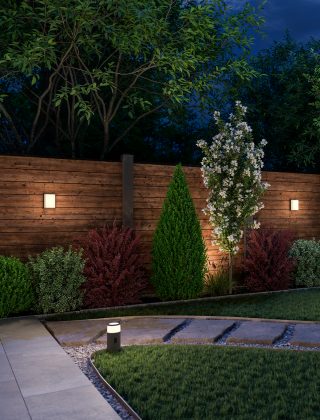 Struiken in de voortuin van een huis, versierd met Festavia LED-netverlichting die in verlopen van roze, paars en wit licht schijnen.