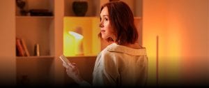 Een vrouw staat in een woonkamer, die wordt verlicht met Philips Hue lampen.