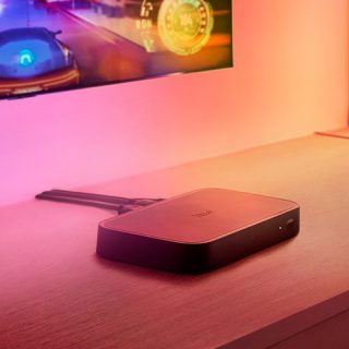 Een Hue Play HDMI sync box onder een tv, verlicht door meeslepende entertainmentverlichting.