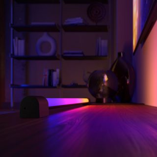 Een Play gradient light tube die onder een tv-scherm is geplaatst en roze, paars en geel licht geeft. 