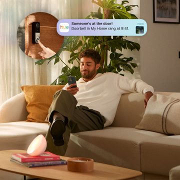 Een man zit op de bank en ontvangt een melding van bewegingsdetectie op zijn smartphone via de Hue app. 