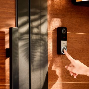 Een vinger die op de knop drukt van een bedrade videodeurbel in een muur