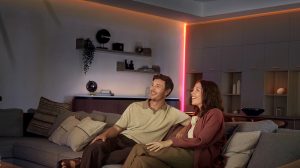 Para siedzi na sofie w salonie, którego narożniki i linie sufitu są oświetlone bezpośrednim światłem z taśmy świetlnej LED OmniGlow. 