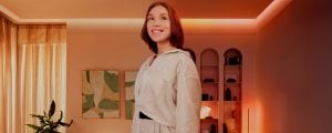 O femeie stă în picioare în camera de zi iluminată cu luminile și lămpile Philips Hue.