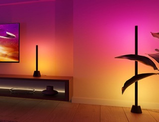 En Philips Hue Play bords- och golvlampa placerade intill en TV och skapar surroundbelysningseffekt i lila, rosa och gula nyanser av ljus. 