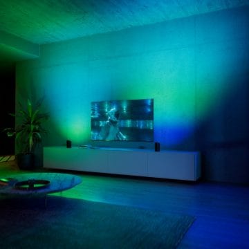 En vägglampa i ett vardagsrum i blått och grönt ljus med två Play wall-washerlampor på båda sidor av en tv. 